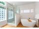 Bright bathroom showcasing a glass enclosed shower, standalone tub with gold fixtures, and unique glass block window at 3028 Rothgeb Dr, Raleigh, NC 27609