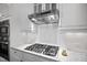 Close up on a gas cooktop set in white marble counters and cabinetry with tiled backsplash at 10523 Bedfordtown Dr, Raleigh, NC 27614