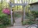 Charming garden gate entrance featuring a wooden arbor, azaleas and natural landscaping at 11009 Eaglerock Dr, Raleigh, NC 27613