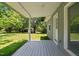 View of the covered porch with wood flooring overlooking the large, green lawn and wooded area beyond at 1661 Reno Sharps Store Rd, Bear Creek, NC 27207