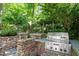 Outdoor kitchen featuring stone accents, a built-in grill, and lush landscaping at 300 Livingstone Dr, Cary, NC 27513