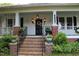 Charming front porch with brick stairs and posts, black railing and door, with decorative planters at 1111 College St, Oxford, NC 27565
