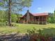 Inviting exterior showcasing a log cabin home with a stone chimney, front porch, and lush yard at 1656 Nc-42 Hwy, Moncure, NC 27559