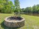 Tranquil outdoor area with a stone fire pit and cooking grate, perfect for gatherings by the pond at 1656 Nc-42 Hwy, Moncure, NC 27559