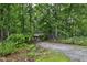View of a lush, treed front yard with a small outdoor building and gravel parking area at 205 Bruton Dr, Chapel Hill, NC 27516