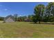 Large grassy backyard featuring mature trees and various buildings in the distance, creating a peaceful outdoor space at 130 Skipwith Dr, Wendell, NC 27591