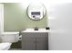 Bathroom features modern vanity, round mirror, and toilet in a room with light green walls at 1316 Garden Crest Cir, Raleigh, NC 27609