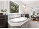 Light-filled main bathroom featuring a soaking tub under a large window, dual sinks, and an open doorway to the main bedroom at 3209 Bryant Falls Ct, Raleigh, NC 27613
