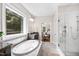 Light-filled main bathroom with soaking tub, glass-enclosed shower, dual sinks, and a view of the lush yard at 3209 Bryant Falls Ct, Raleigh, NC 27613