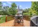 Outdoor deck featuring a table with chairs, umbrella, grill, and a lush backyard view at 401 Clingstone Ct, Cary, NC 27519