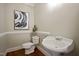 Stylish powder room featuring a pedestal sink, toilet, and a modern art piece enhancing its appeal at 4812 Cornoustie Ct, Holly Springs, NC 27540