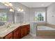 Bathroom featuring double sinks, wooden cabinets, a large mirror, and a separate soaking tub at 1028 Bellenden Dr, Durham, NC 27713