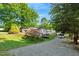 Charming home exterior featuring a well-manicured lawn, flowering shrub, and gravel driveway surrounded by lush greenery at 135 Sagamore Dr, Louisburg, NC 27549