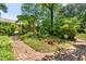 Landscaped backyard featuring a brick pathway winding through mature trees and lush greenery, enhancing natural beauty at 2143 Ridge Rd, Raleigh, NC 27607