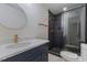 Bathroom with blue vanity, gold fixtures, round mirror, and glass door shower with black tiling at 4713 Erwin Rd, Durham, NC 27705