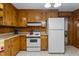 A white refrigerator and stovetop compliment the wood paneled walls and cabinets of this compact kitchen at 5517 Spring Rd, Raleigh, NC 27603