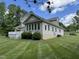 The manicured lawn leads to the beige home, featuring a sunroom and deck, all under a sunny sky at 84 Macbeth Ln, Roxboro, NC 27574