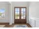 Elegant foyer showcasing double glass doors, wainscoting, and hardwood flooring at 8416 Brady Pointe Rd, Fuquay Varina, NC 27526