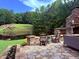 Stone patio with fireplace, overlooking water feature, green hills, and lush landscaping at 233 Hein Dr, Clayton, NC 27527