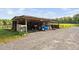 Open shed with gravel floor and various storage items, adjacent to fenced pasture and lush greenery at 3123 Brassfield Rd, Creedmoor, NC 27522