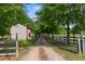 Long, gravel driveway leading to a barn, framed by mature trees and white fencing at 5237 Christian Light Rd, Fuquay Varina, NC 27526