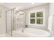 Bright bathroom features a glass-enclosed shower and soaking tub under a window overlooking a private yard at 5180 Old Powell Rd, Holly Springs, NC 27540