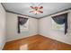 Cozy bedroom with hardwood floors, ceiling fan, and two windows with decorative curtains at 5652 Laurel Crest Dr, Durham, NC 27712