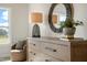 Bedroom showcasing a dresser with a stylish lamp and a round mirror, complemented by a comfortable chair and a window at 702 Beacon Hill Rd # 51, Lillington, NC 27546