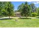 View of a well-maintained front yard with mature trees and a charming brick home in the background at 827 Loop Rd Rd, Burlington, NC 27217