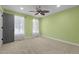 An empty light green bedroom is carpeted and has two windows, white sheer curtains and a gray door at 3216 Green Valley Dr, Sanford, NC 27330