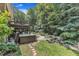 View of backyard featuring an elevated deck, jacuzzi, rock water feature, lush trees and landscaping at 10909 Raven Rock Dr, Raleigh, NC 27614