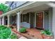 Covered front porch featuring classic columns, brick flooring, a wooden front door, and a cozy seating area at 1513 Dellwood Dr, Raleigh, NC 27607