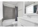 Bright bathroom features a gray tiled shower, white vanity, and large mirror by the window at 320 Chickasaw Plum Dr, Holly Springs, NC 27540