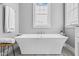 Freestanding bathtub with modern fixtures beneath a sunny window and grey walls at 320 Chickasaw Plum Dr, Holly Springs, NC 27540