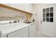 Functional laundry room with modern washer and dryer units, shelving, and an exterior door at 1025 Kingsway Dr, Apex, NC 27502