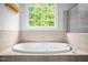 Close up of a white garden tub with tile surround and window overlooking lush greenery at 4874 Thom Rd, Mebane, NC 27302
