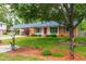 Charming single-story home with a red door, landscaped front yard, mature trees, and a covered carport at 1209 Maple Ave, Apex, NC 27502