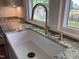 Close-up of a white farmhouse sink, granite counter, and brass faucet by a bright window at 2227 Us-15, Creedmoor, NC 27522