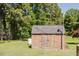 A wooden shed with a shingled roof surrounded by trees and a well-maintained lawn offers outdoor storage at 64 Red House Rd, Smithfield, NC 27577