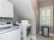Laundry room with white cabinets, washer, dryer, window with shutters and tile floor at 124 Creekvista Dr, Holly Springs, NC 27540