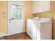 Functional laundry room with white appliances, upper cabinets, and a glass paneled door leading to the backyard at 3123 Amherst Ave, Burlington, NC 27215