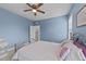 Light-filled bedroom with blue walls featuring a cozy bed, ceiling fan, and ample natural light from the windows at 348 Golf Vista Trl, Holly Springs, NC 27540