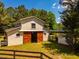 Barn exterior featuring wooden doors and a paddock entrance, surrounded by lush greenery and a wooden fence at 815 Solitude Pt, Chapel Hill, NC 27516