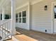 Home's covered porch showcasing natural wood flooring, white posts, and an exterior light fixture at 4016 Berman Edge Rd, Holly Springs, NC 27540