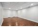 Finished basement with hardwood floors and white walls features a drop ceiling and two doors for storage at 7808 Umstead Forest Dr, Raleigh, NC 27612