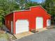 Side-angle view of a new red metal barn featuring multiple garage doors and a gravel parking area at 121 Pheasant Ct, Pittsboro, NC 27312