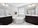 Bright bathroom featuring a soaking tub, white tiling, and dark brown double vanity sinks at 1458 Wragby Ln, Apex, NC 27502