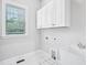 Bright laundry room with white cabinets, tiled floors, and natural light from the window at 203 S South Bend Dr, Durham, NC 27713