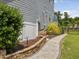 Exterior side view showcasing walkway with stone retaining wall and lush landscaping at 213 Lofty Oak Ln, Holly Springs, NC 27540