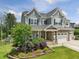 Two-story home featuring gray siding, a stone-accented garage, and a charming covered front porch at 213 Lofty Oak Ln, Holly Springs, NC 27540